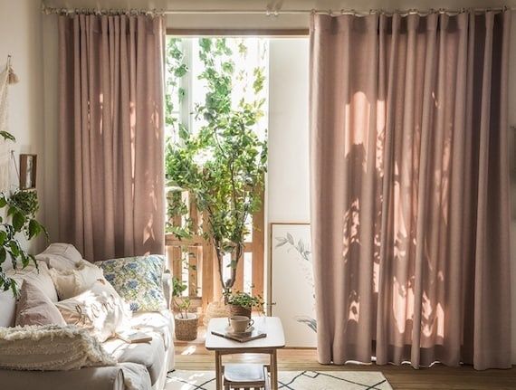 Lys stue med tunge gardiner, sofa, planter og trægulv